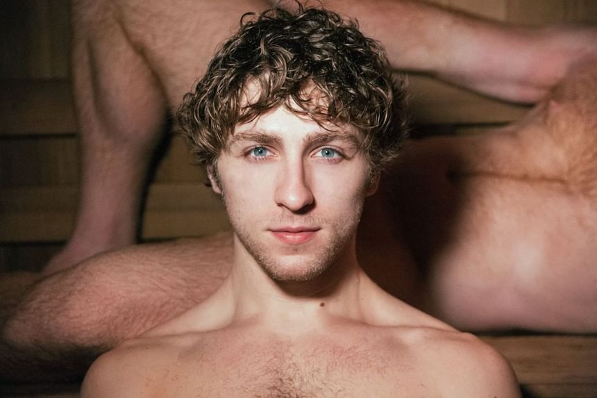 A young person sits in a sauna, with a wooden backdrop showcasing a relaxed, intimate atmosphere at The Gaythering