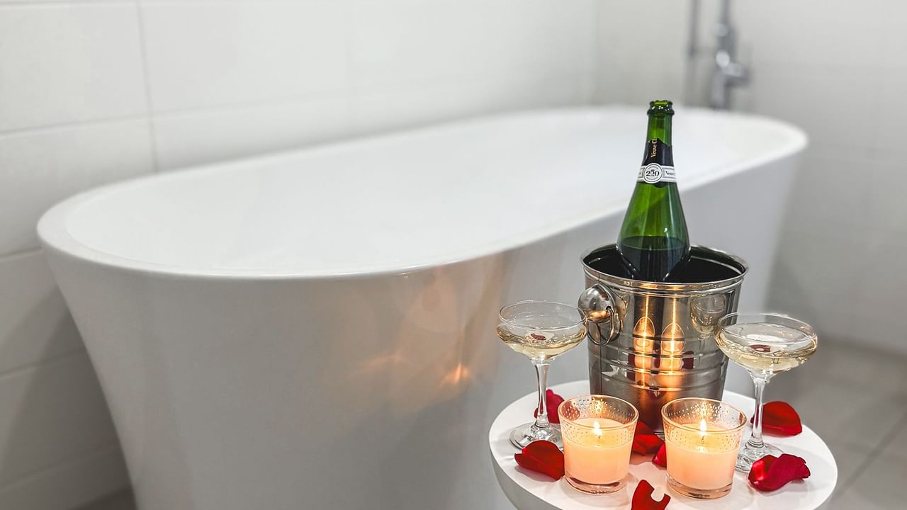 Bathtub and a small table holding a wine bottle, two wine glasses, and two candles.