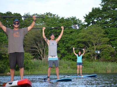Three people on paddleboards in a calm lake, holding paddles overhead near Breezeway Boutique Hotel