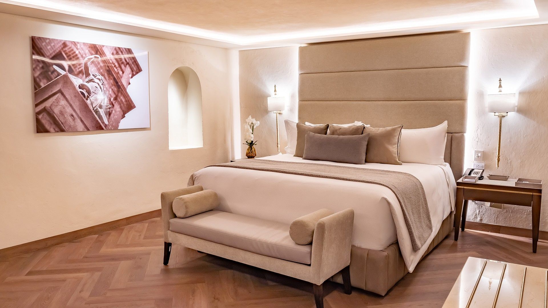 King Grand Class Suite with a cozy bed, a tan headboard, a matching bench, and white orchid centerpiece at Quinta Real Puebla