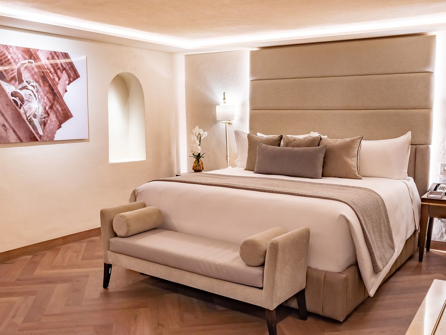 Habitación de hotel con cama grande, sofá, mesas de noche, y pintura en la pared.