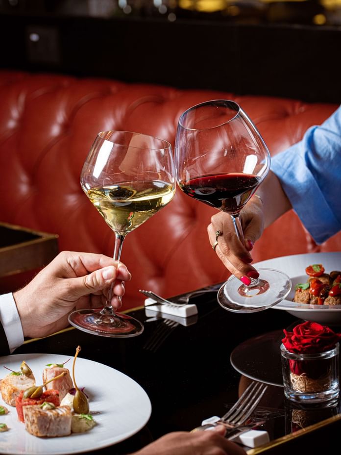 Two elegantly dressed hands clink glasses of white and red wine in a romantic setting at The Republic Hotel