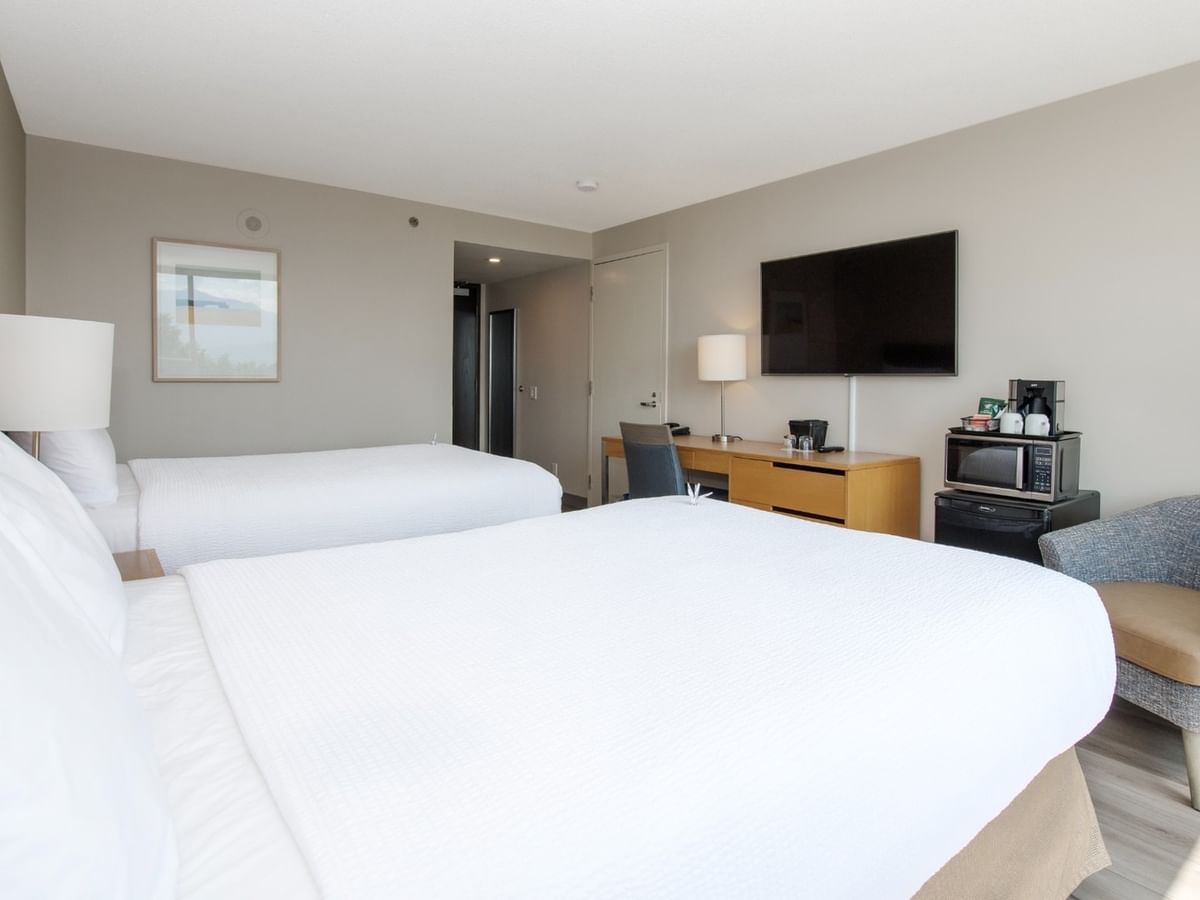 Two beds, chair, desk, TV, lamp, microwave and mini fridge in a hotel room.