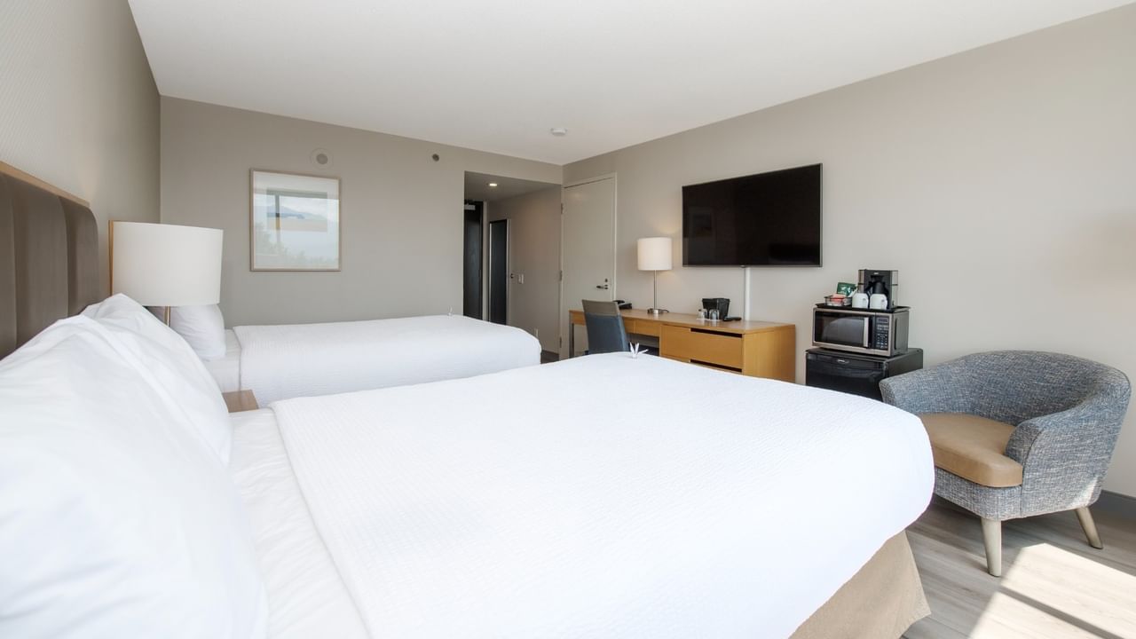 Two beds, chair, desk, TV, lamp, microwave and mini fridge in a hotel room.