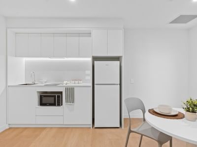 White kitchen with refrigerator, microwave, and dining area at UniLodge Brisbane City.