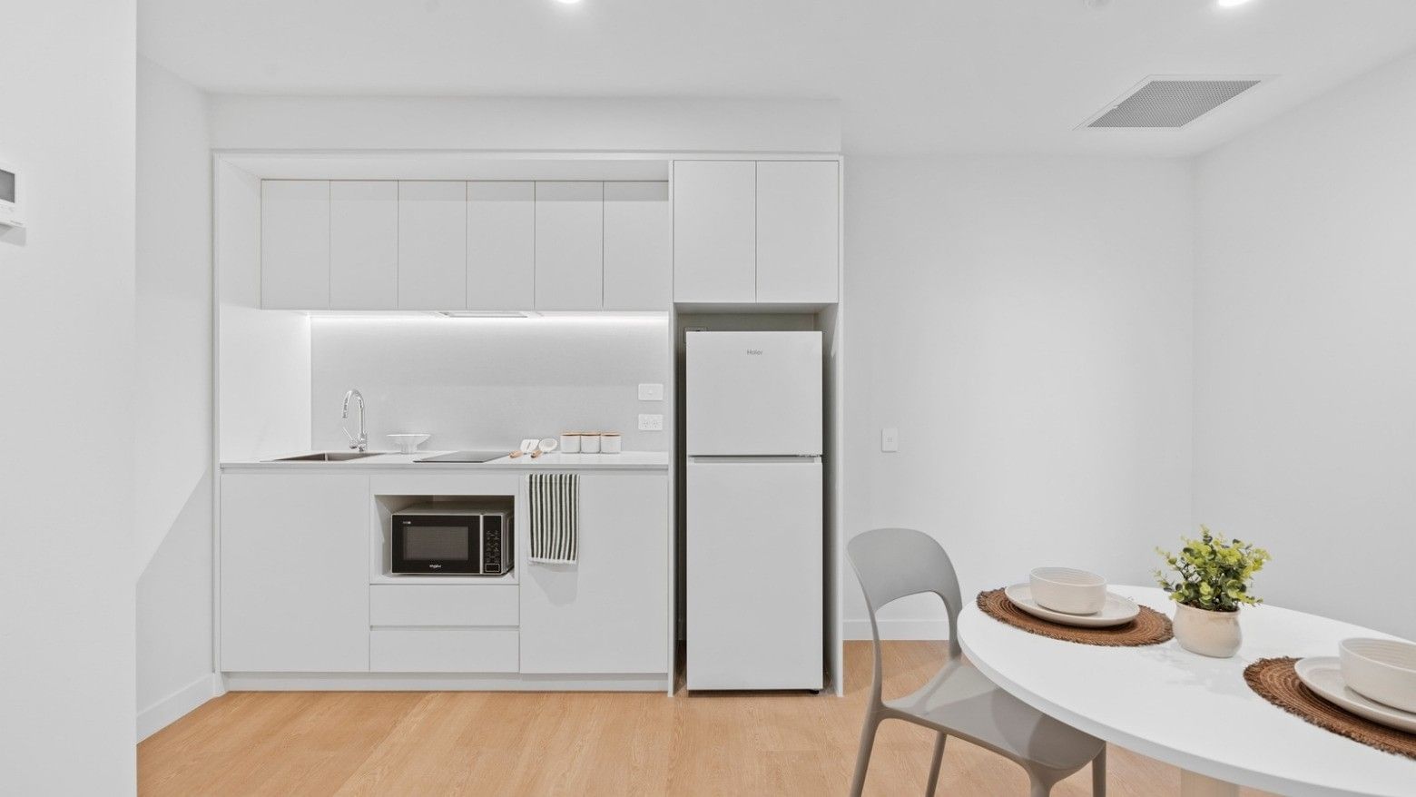 White kitchen with refrigerator, microwave, and dining area at UniLodge Brisbane City.