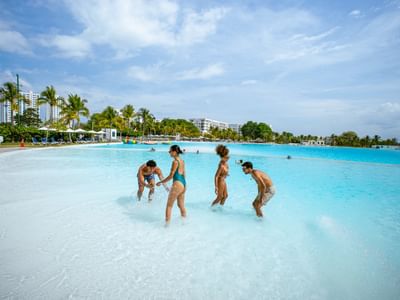 Family playing in expansive turquoise pool surrounded by palm trees and resort buildings at Playa Blanca Beach Resort