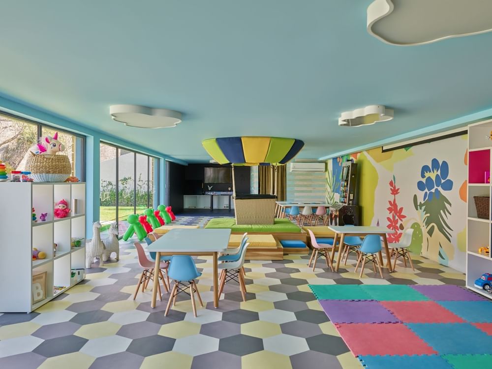 Kids lounge room with play mats, dining tables & shelf with toys at Live Aqua Resorts and Residence Club