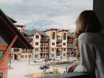 Guest enjoying mountain view from balcony overlooking alpine resort village with snow-capped peaks in the distance.