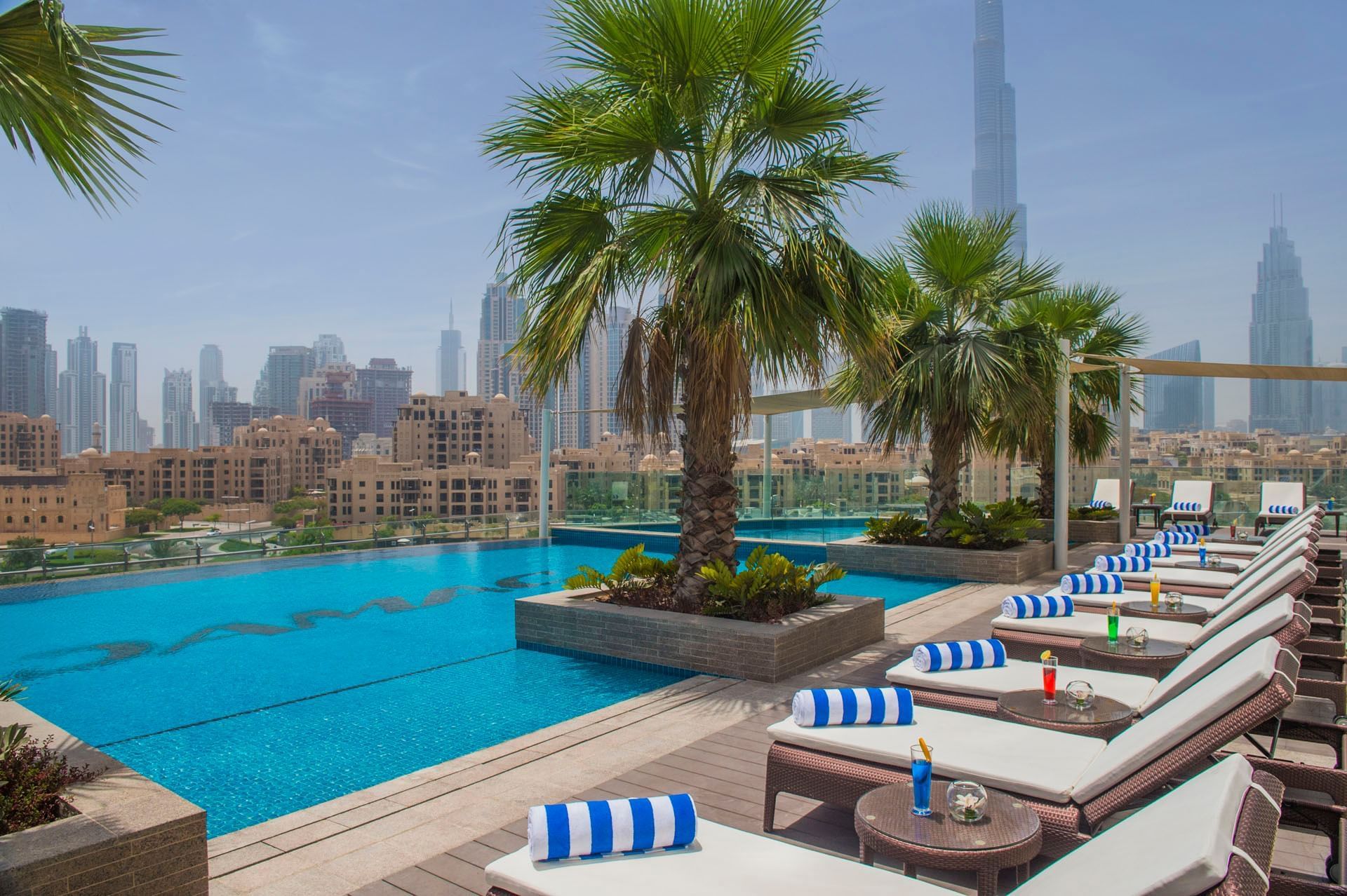 An outdoor pool on a terrace with sun loungers near palm trees at DAMAC Maison Distinction