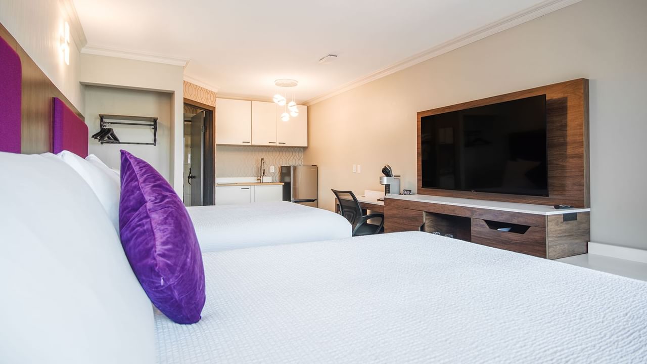 Hotel guest room with two queen beds, a kitchenette, flat screen TV, and work desk