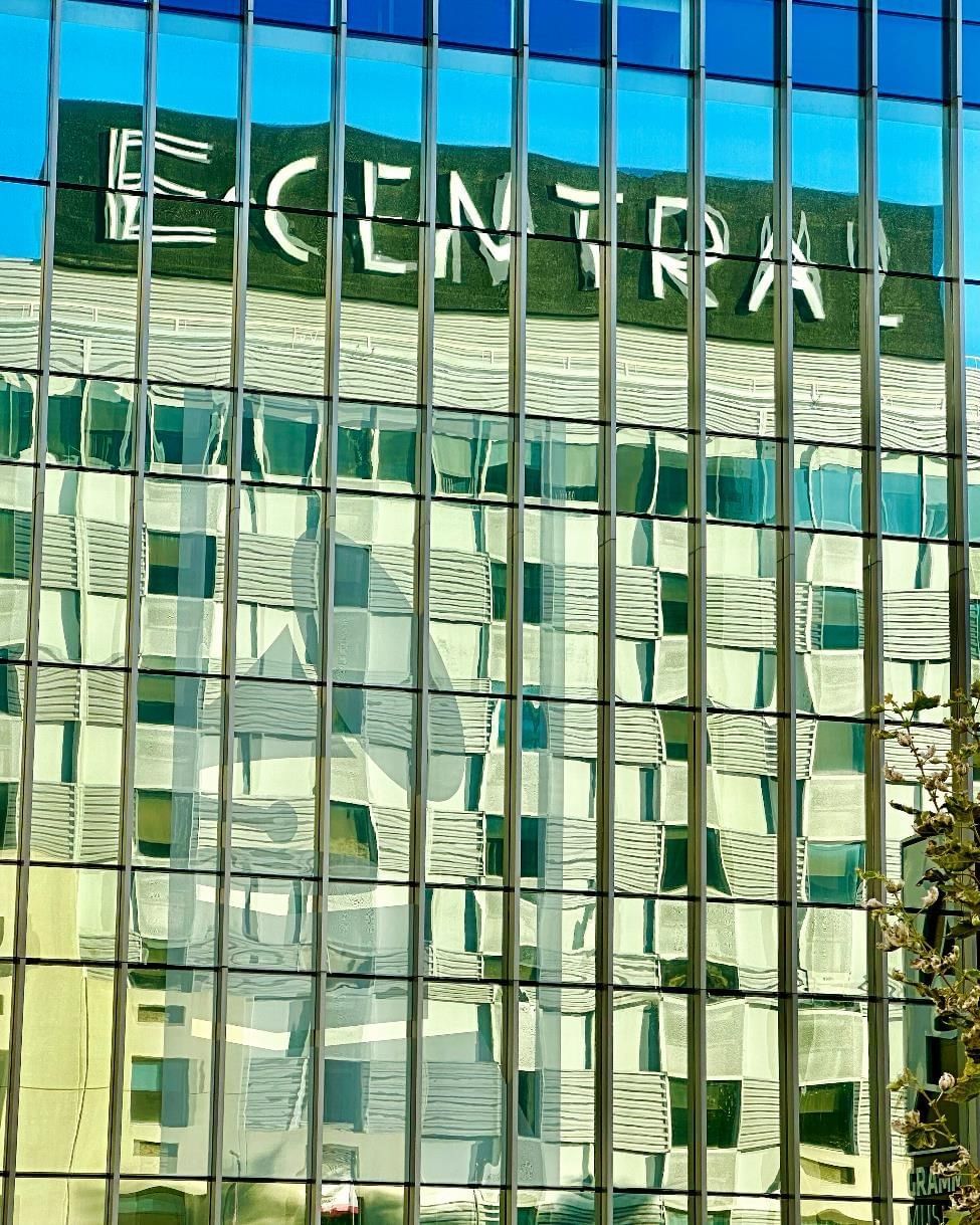 A close-up of a building's exterior with a glass facade reflecting the sky and showing the hotel's name in large letters.