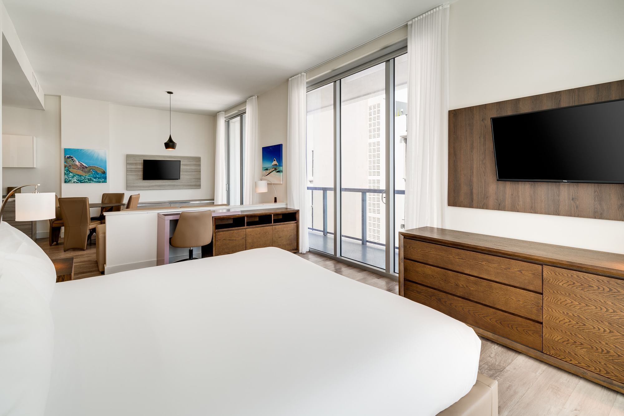 A wide view of a modern hotel room with a large bed, desk area, and balcony door.