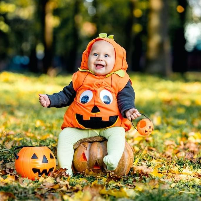 A baby dressed up as a pumpkin in a park city near Stein Lodge