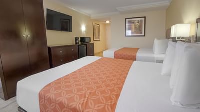 Two beds by a wood dresser in Double Queen Room at Galleria Palms Hotel, an affordable hotel near Disney World for families