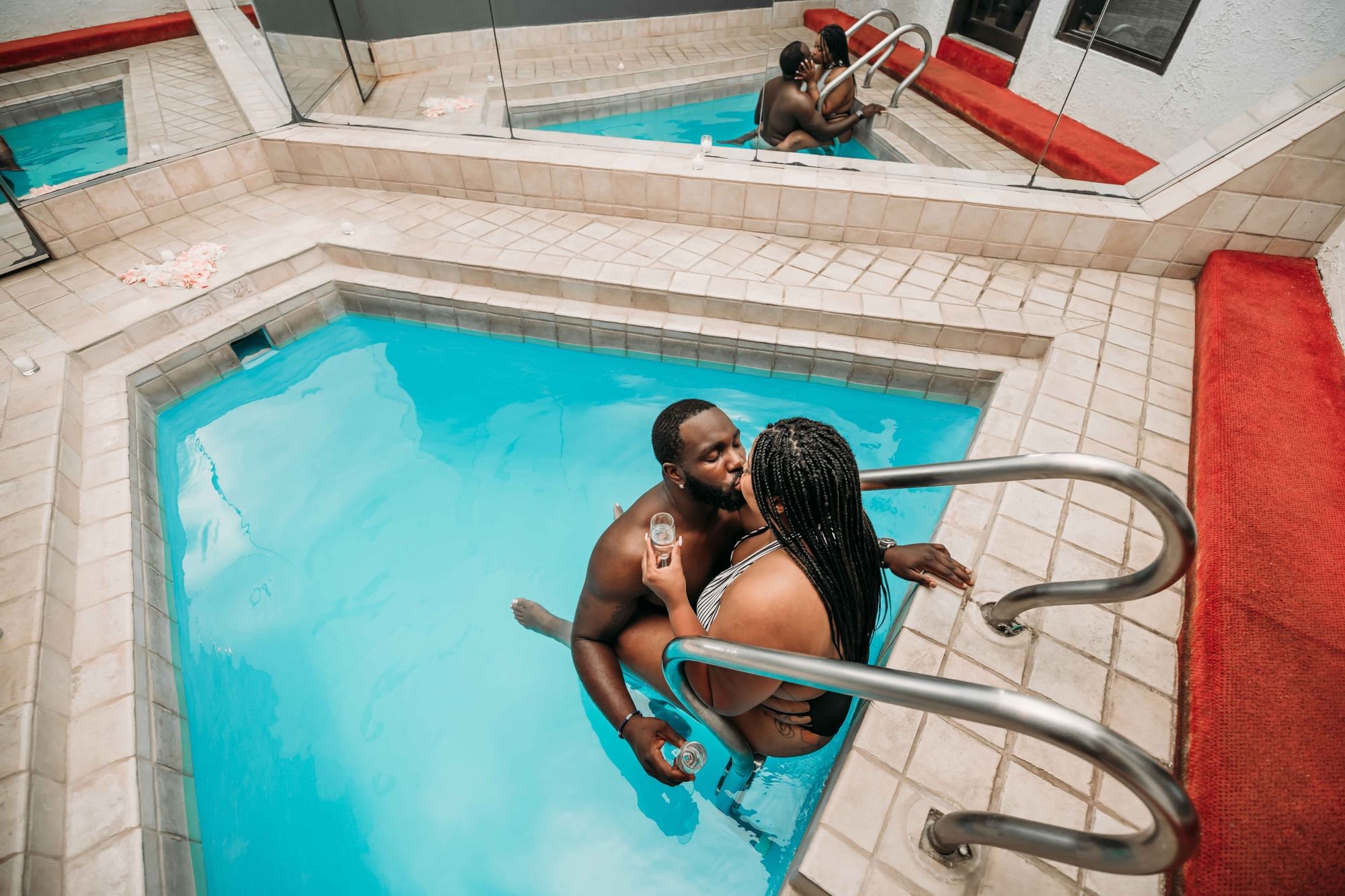 Couple in a pool, kissing and holding glasses, surrounded by mirrored walls at Cove Pocono Resorts