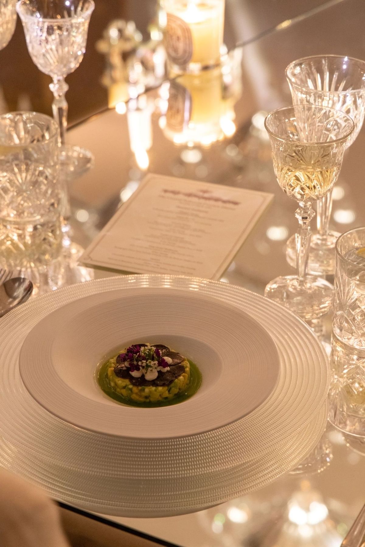 White plate with dish, wine glasses, and menu card on glass table at The May Fair Hotel London