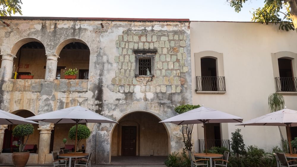 Edificio de piedra con sombrillas blancas en café al aire libre en plaza soleada en Quinta Real Oaxaca