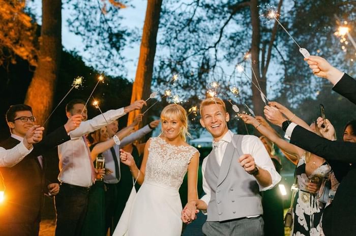 Bride and groom surrounded by their wedding guests holding sparklers at Gorse Hill in Surrey