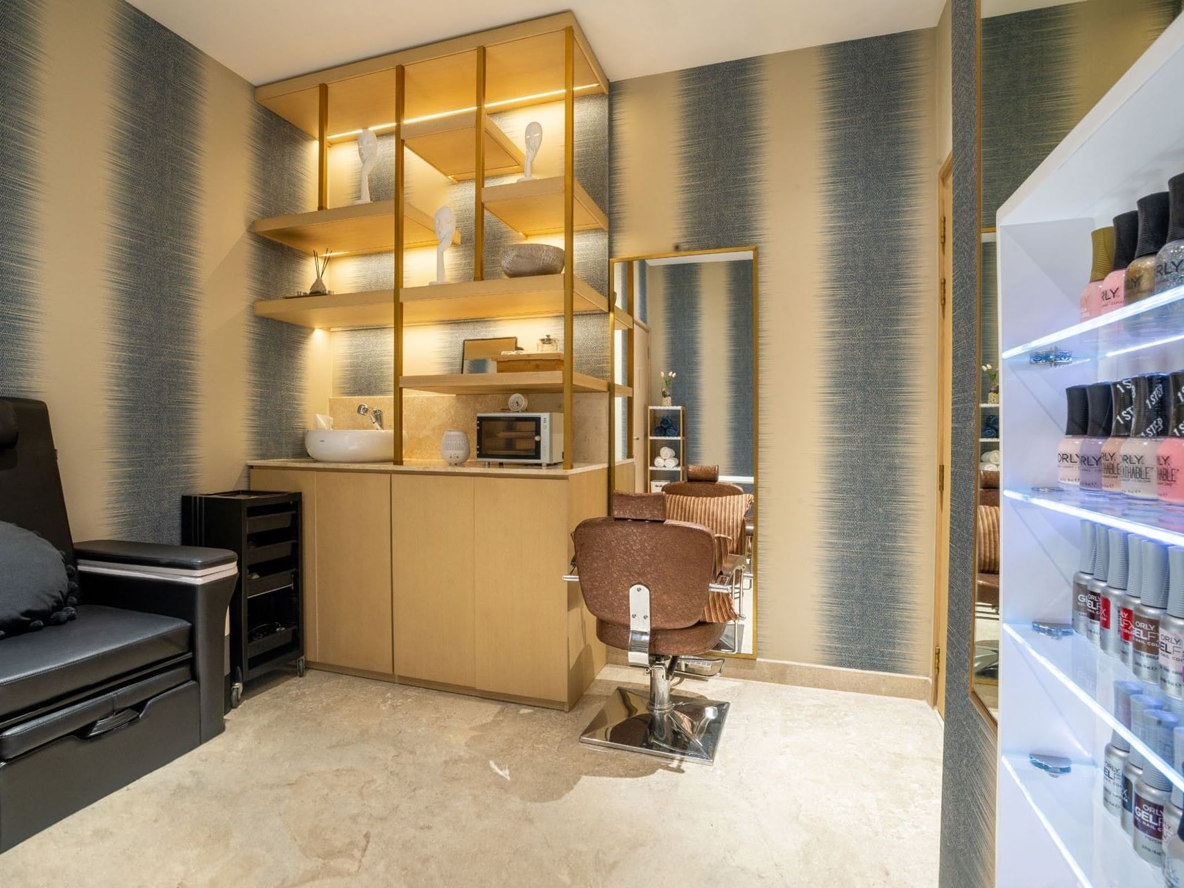A salon with a chair, shelves, a sink, a microwave, and a display case filled with nail polish.