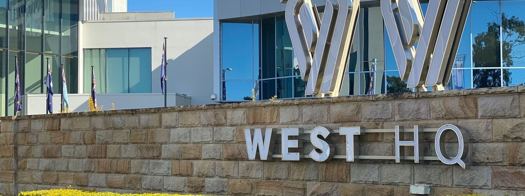 Entrance of Novotel Sydney with West HQ sign on a stone wall, metallic W sculptures, greenery, and a sleek glass façade