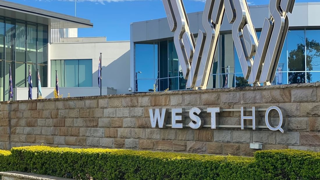 Entrance of Novotel Sydney with West HQ sign on a stone wall, metallic W sculptures, greenery, and a sleek glass façade