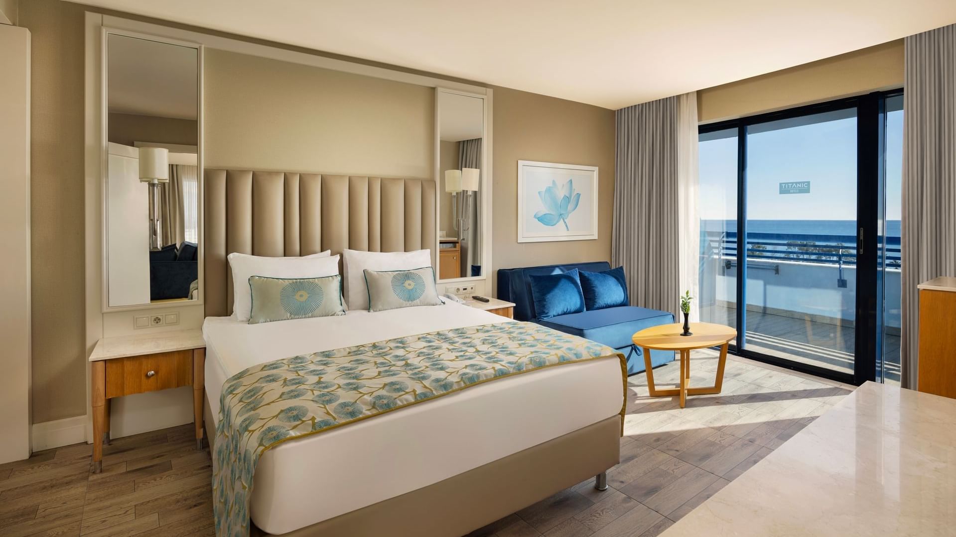 Colonel Suite features a plush bed with blue accents, a blue sofa, a wooden table, and large window at Titanic Deluxe Lara