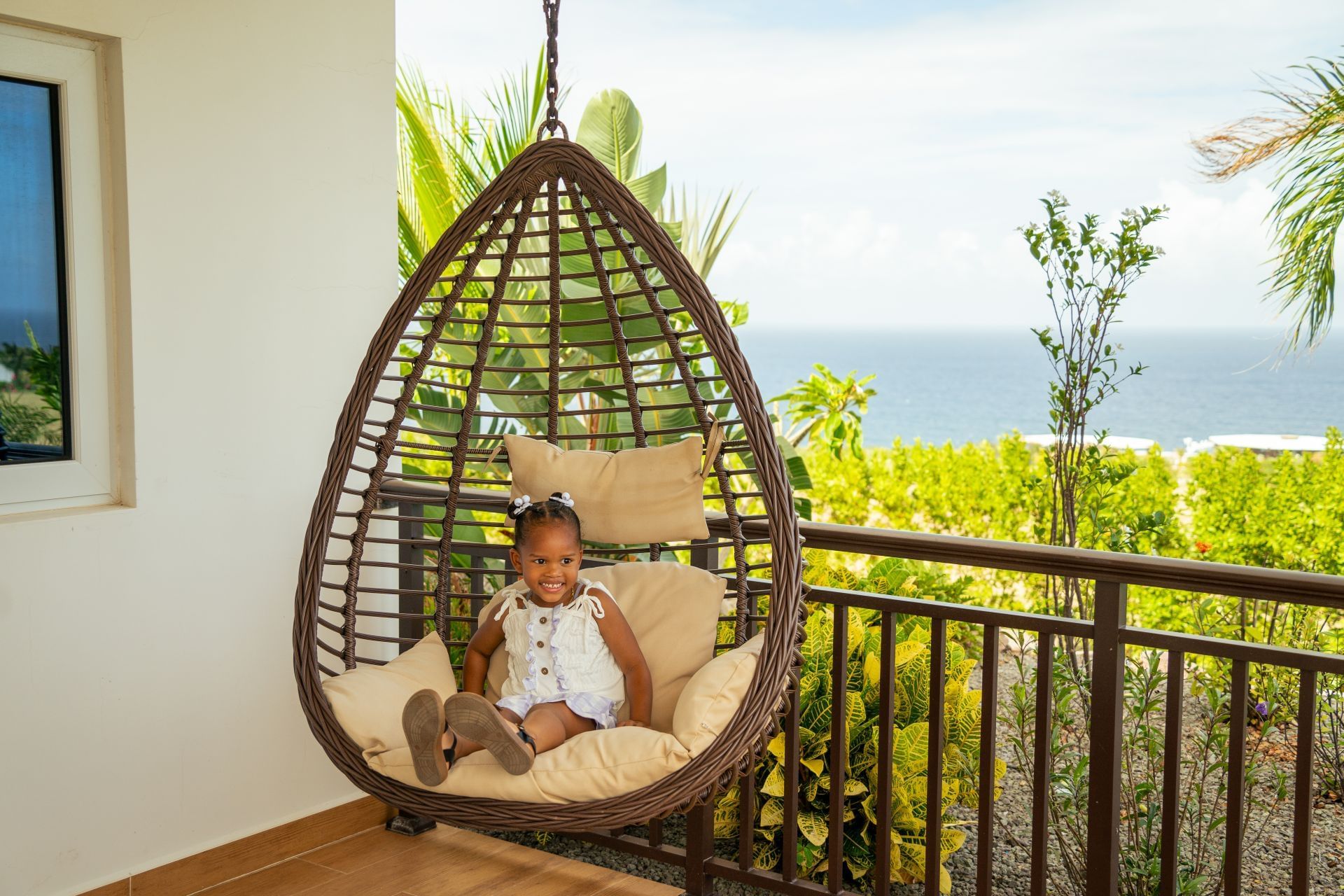Kind ontspant in een hangende schommelstoel op een balkon met uitzicht op het groen en de oceaan in Golden Rock Resort