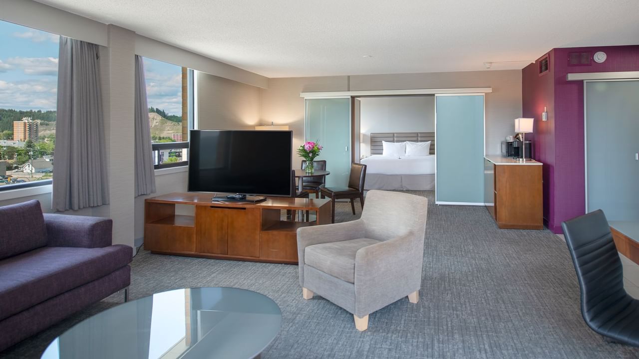 Hotel suite with living area, bedroom, and windows with views.