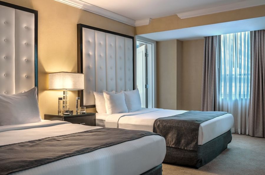 Two queen beds with white linens and brown blankets in a Premium Suite at Warwick Allerton Chicago