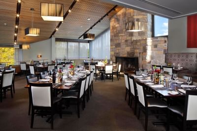 Multiple long tables set with white plates, wine glasses, and flowers in a dining room at Chauncey Conference Center.