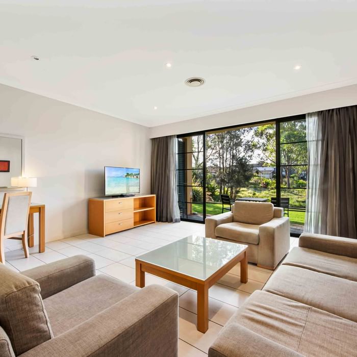 Three Bedroom Apartment living room with a lake view through large windows, sofas, and a TV at Mercure Kooindah Waters