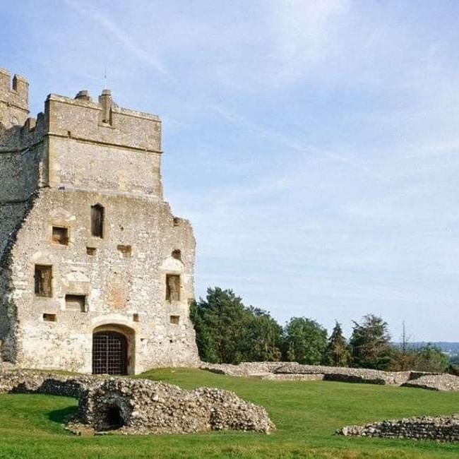 Stone ruins of Donnington Castle with arched entrance and surrounding greenery under a blue sky.