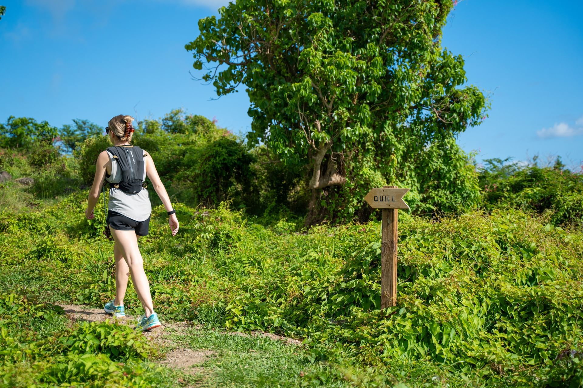 Vrouw in sportkleding die over een weelderig pad loopt met een houten bord dat naar de Quill wijst nabij Golden Rock Resort