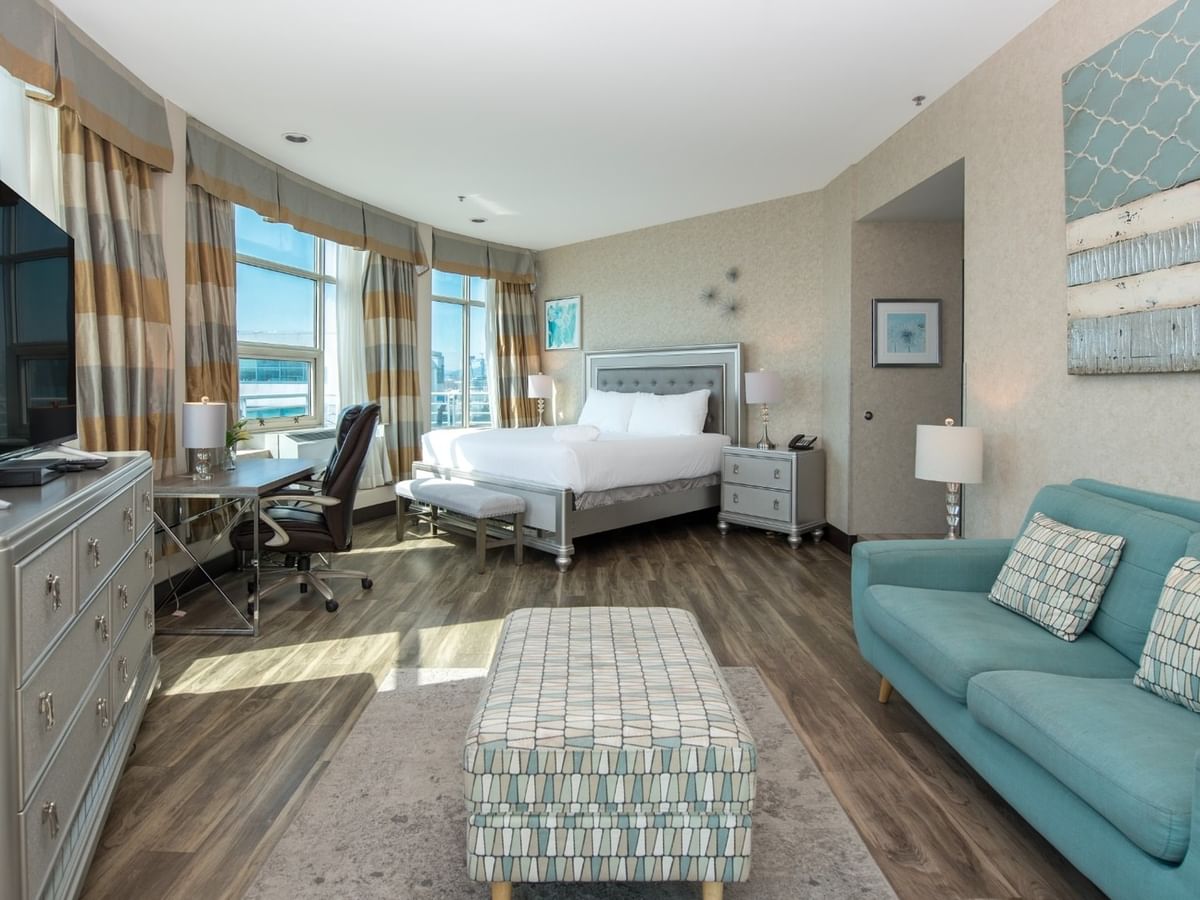 Coast Waterfront Suite with a bed, couch, dresser, desk, TV, and large windows at Coast Lonsdale Quay Hotel