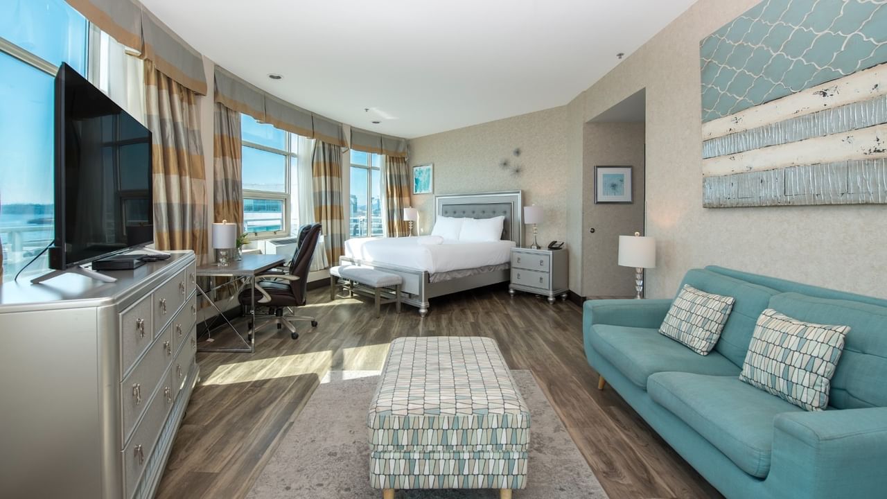 Coast Waterfront Suite with a bed, couch, dresser, desk, TV, and large windows at Coast Lonsdale Quay Hotel