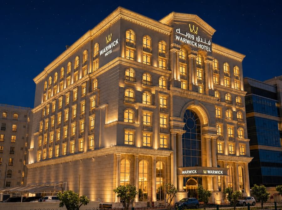Illuminated Warwick Doha Hotel at night with many glowing windows and decorative lighting.