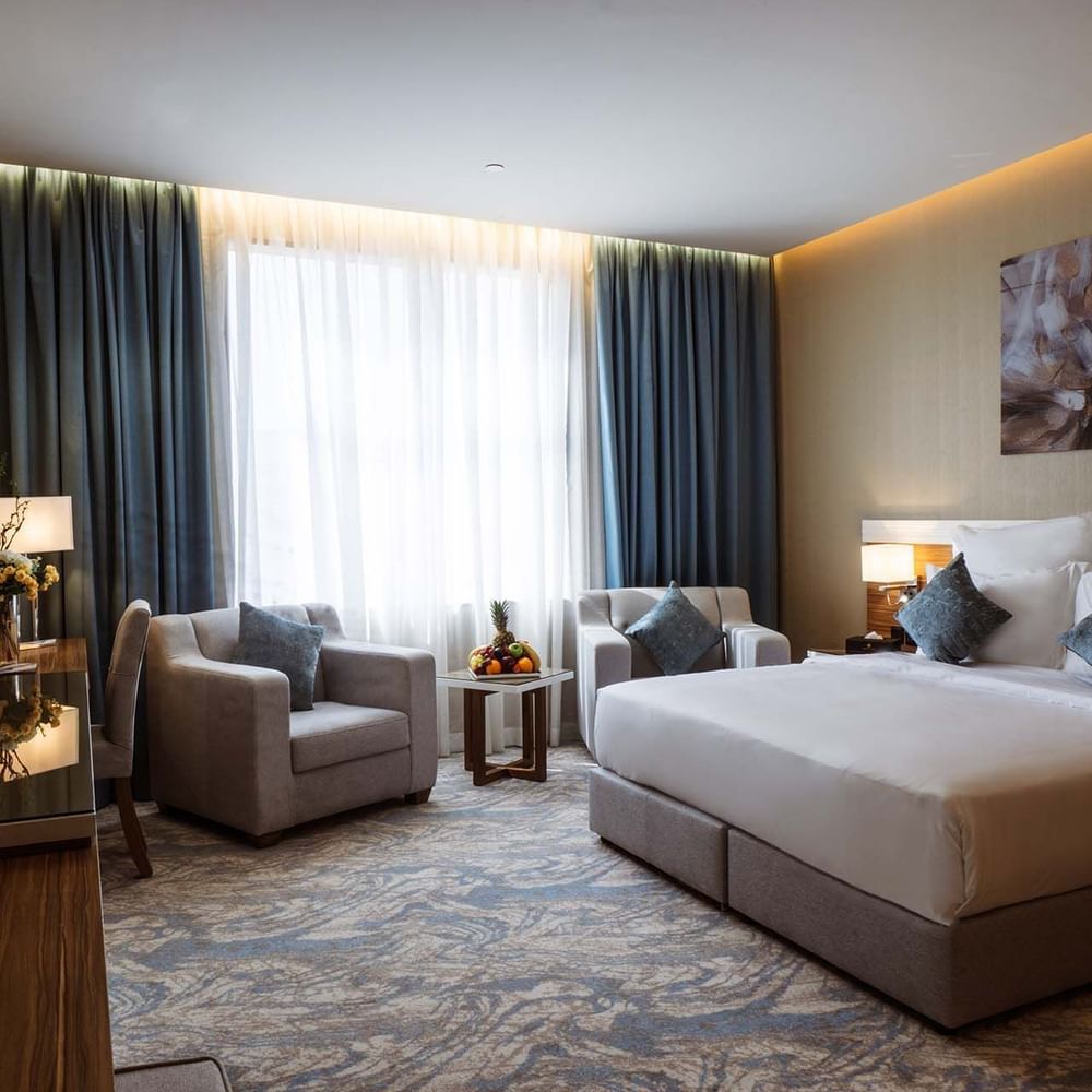 Large bed with armchairs by a fruit tray under a large window in Standard King Room at Cantonal Hotel by Warwick Riyadh