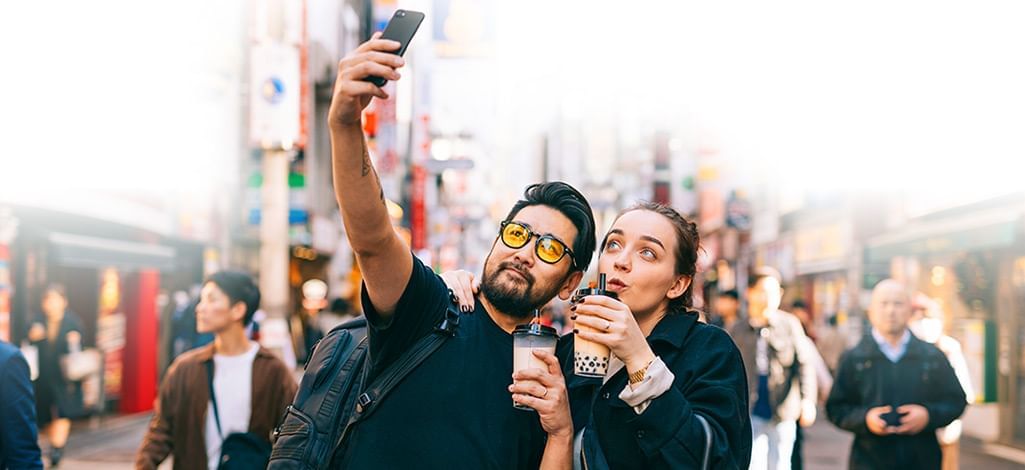 Two people taking a selfie on a bustling street in Japan