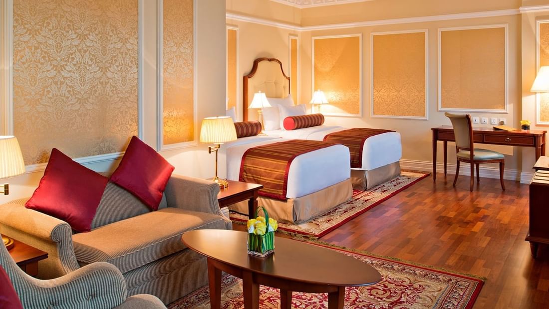 Cozy bedroom featuring double beds & lounge area in Junior Suite at Warwick Doha