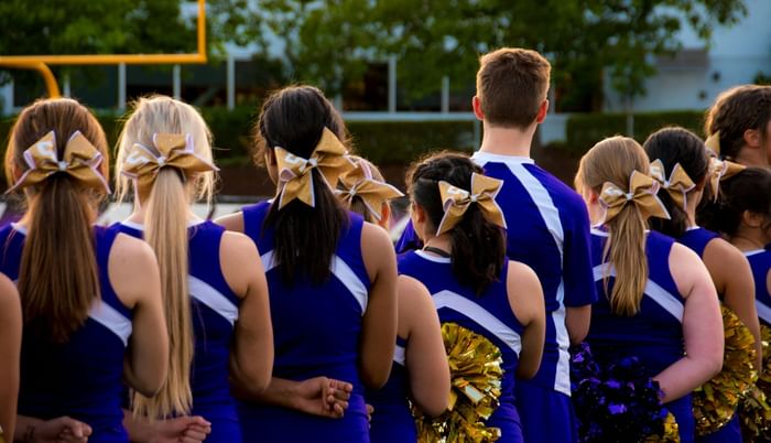 Cheerleaders in blue uniforms standing by a field under trees near Anaheim Portofino Inn & Suites