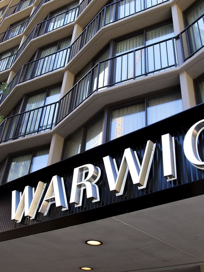 The Warwick Seattle hotel entrance features a large black sign under the balcony