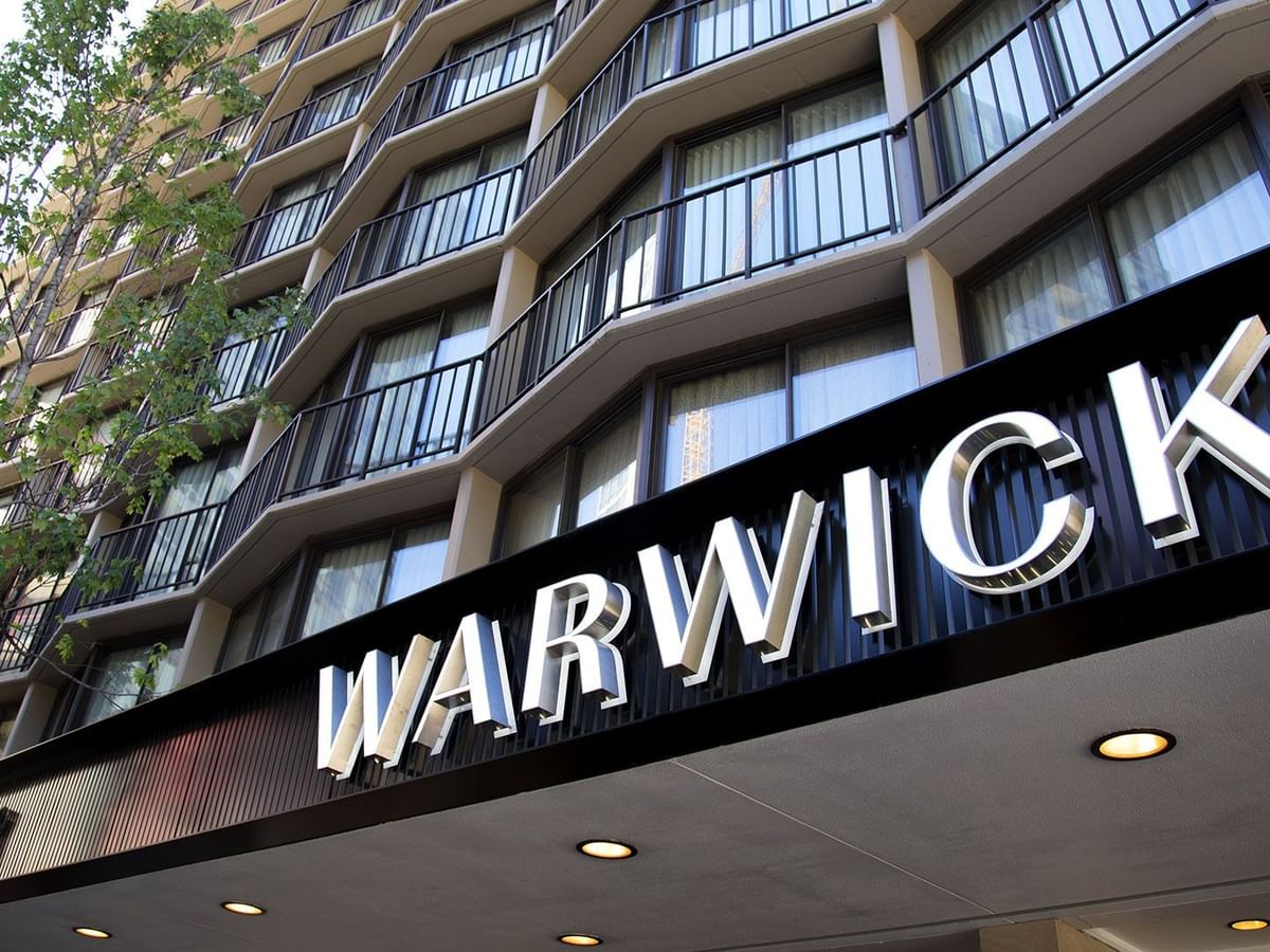 The Warwick Seattle hotel entrance features a large black sign under the balcony