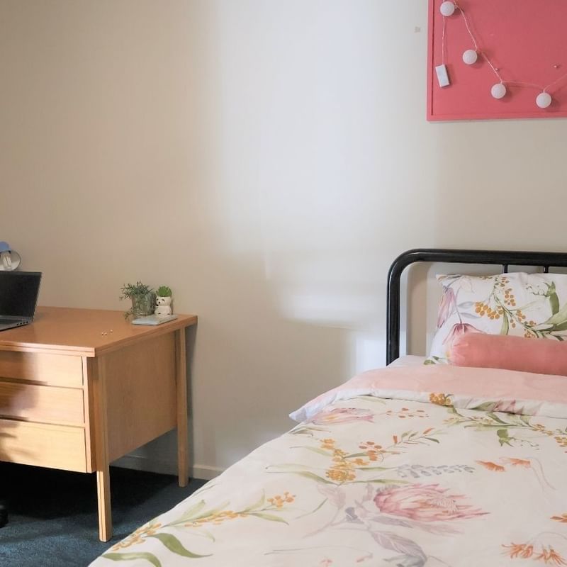 Comfortable bed with floral sheets and desk with laptop at La Trobe University Villas.
