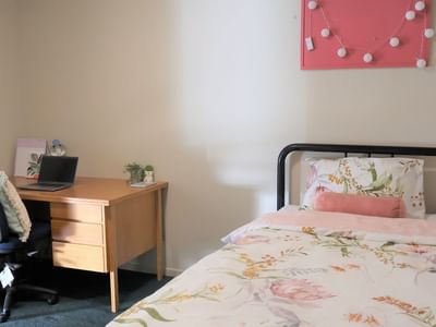 Comfortable bed with floral sheets and desk with laptop at La Trobe University Villas.