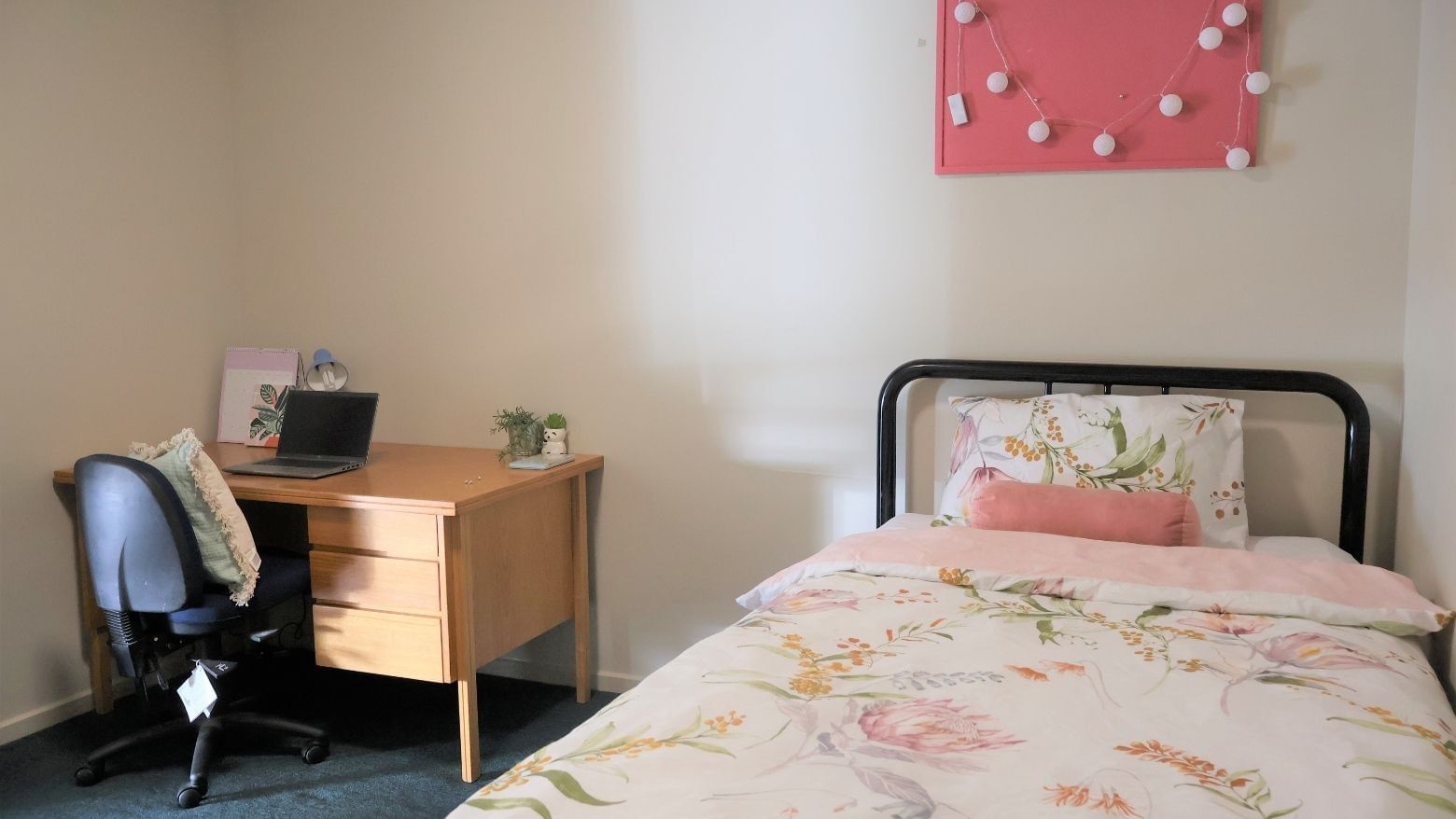 Comfortable bed with floral sheets and desk with laptop at La Trobe University Villas.