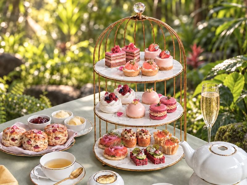 Elegant three-tier stand with pink pastries, scones, and tea service displayed on an outdoor table surrounded by lush greenery at The Banjaran Hotsprings Retreat celebrating Pink October