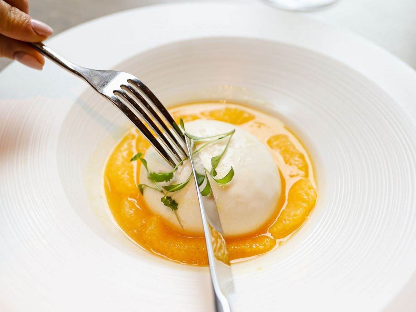 Person holding fork over a poached egg with a garnish at The Londoner Hotel