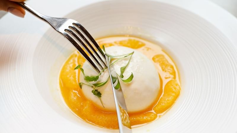 Person holding fork over a poached egg with a garnish at The Londoner Hotel