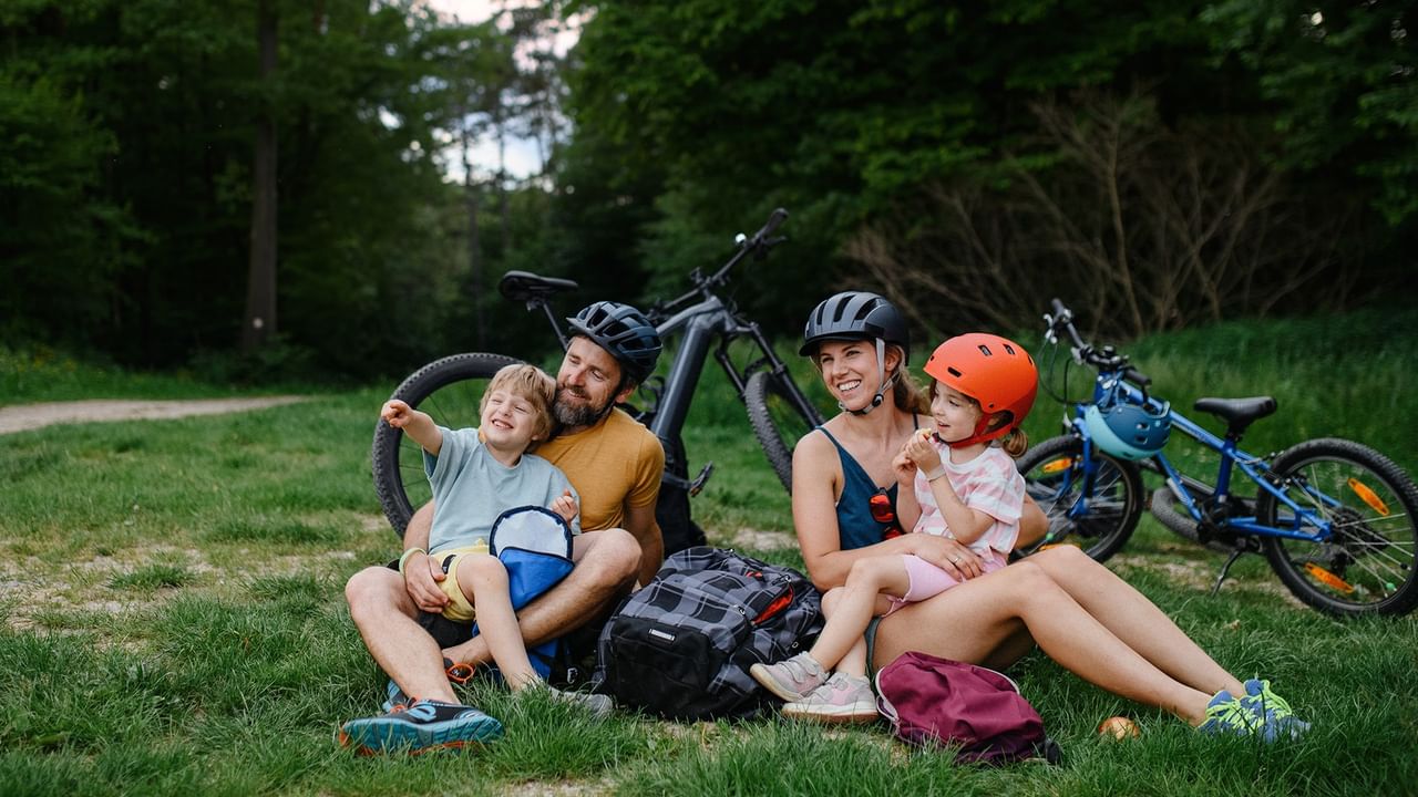 Family enjoying outdoor activity with bikes and helmets on a grassy area.